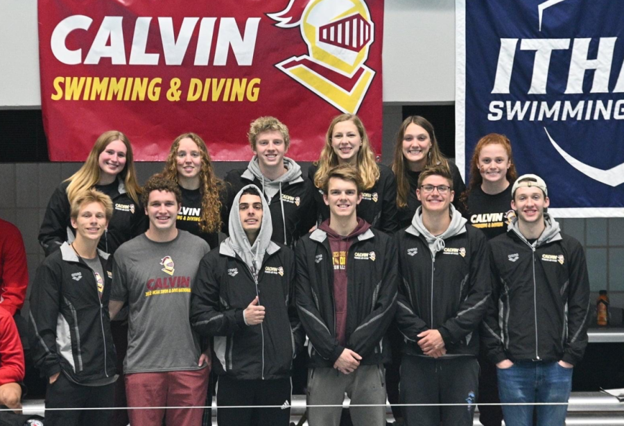 The swim team poses in front of a Calvin flag